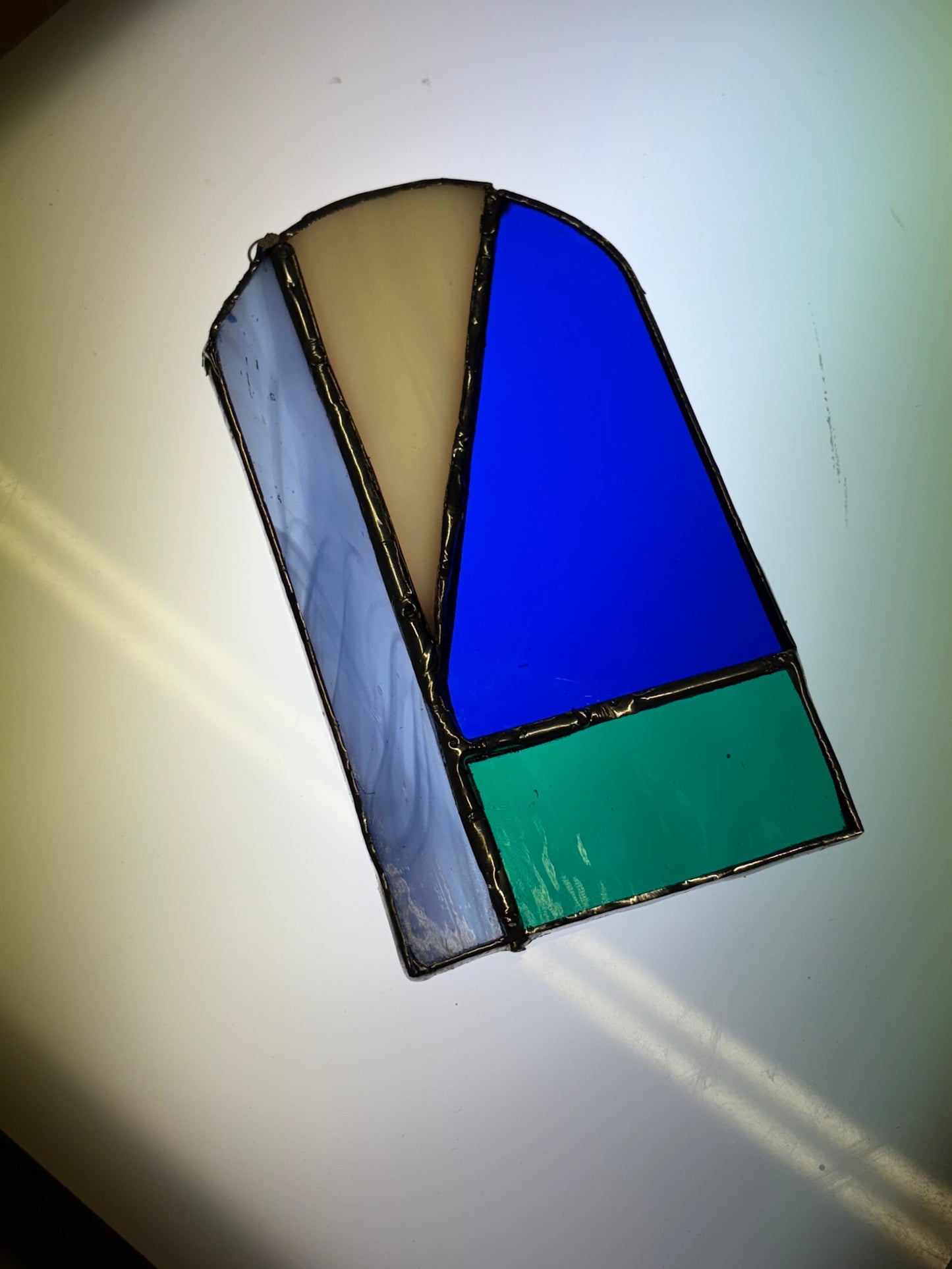 A piece of stained glass piece with blue, green, light blue and yellow colours 